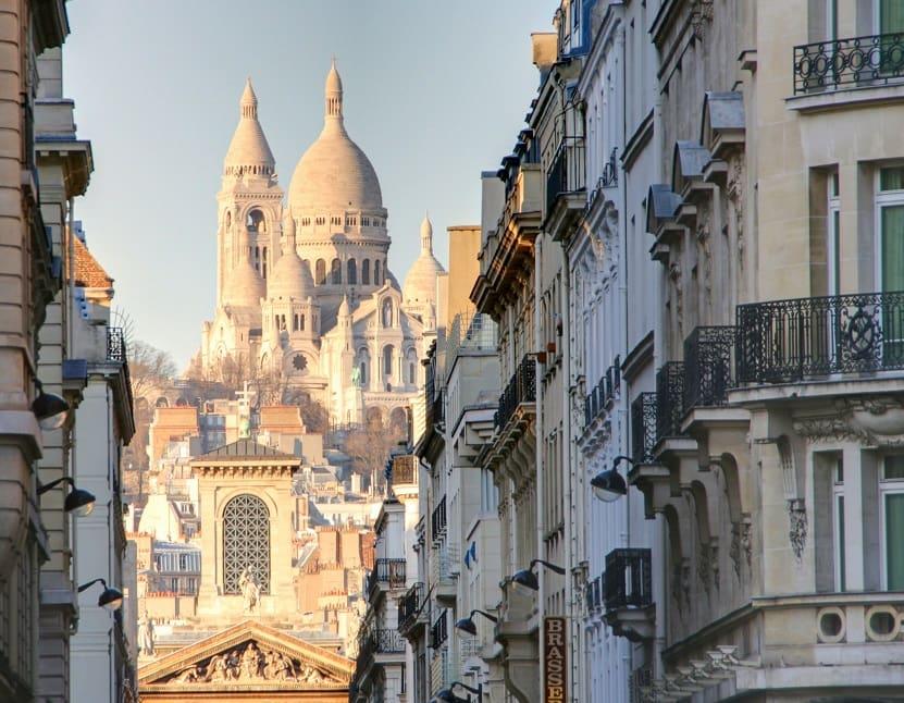 Calle estrecha de Montmartre con edificios Haussmann llevando hacia la Basílica del Sagrado Corazón en París.
