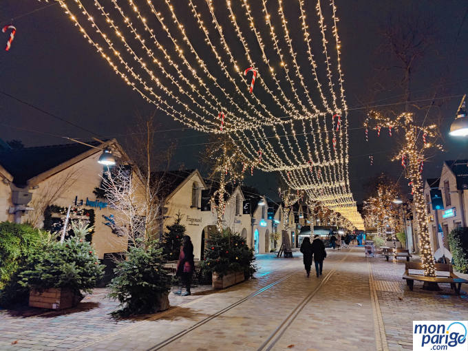Calle peatonal de Bercy Village con tiendas y restaurantes decorada con luces y bastones de Navidad