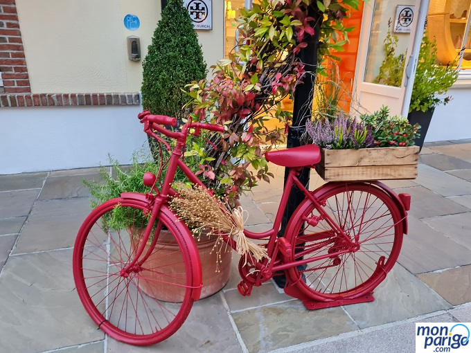 Tiestos con flores y una bici de acero roja frente a una tienda del outlet de La Vallée Village junto a Disneyland Paris