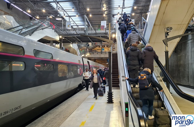 Pasajeros saliendo de un tren de alta velocidad TGV y caminando hacia las escaleras mecánicas de la estación