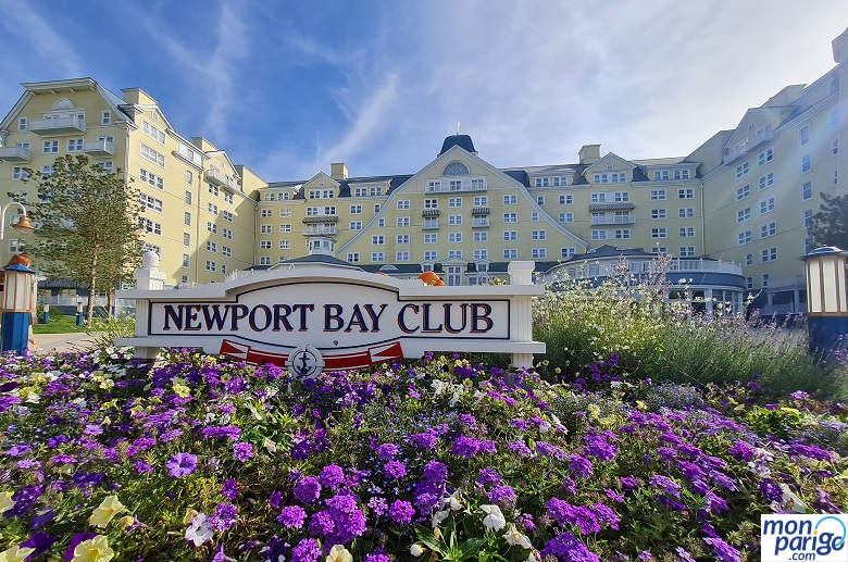 Flores y un cartel que indica Newport Bay Club frente a la fachada principal del hotel