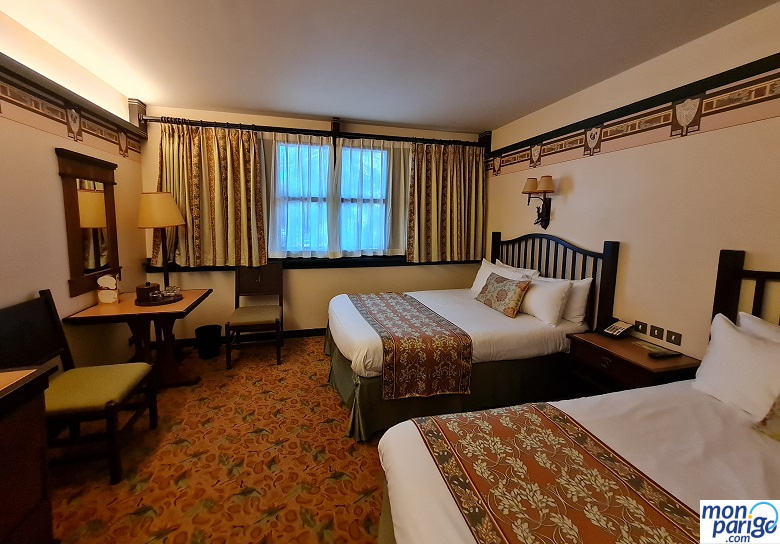 Habitación con dos camas de matrimonio, suelo de moqueta, mesa y sillas en el hotel Sequoia Lodge de Disneyland Paris