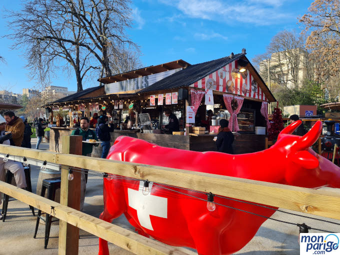 Caseta de madera que vende comida y bebida en Navidad junto a una vaca con la bandera de Suiza