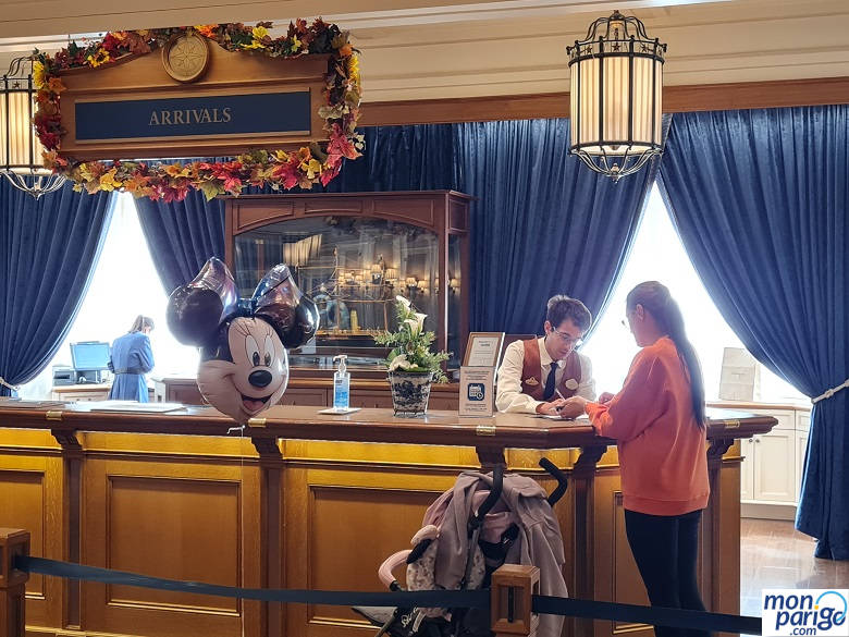 Mostrador de la recepción del hotel Newport Bay Club de Disneyland Paris con un chico atendiendo a una clienta con un carro y un globo de Minnie