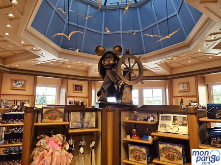 Regalos y souvenirs a la venta junto a una escultura de Mickey sujetando un timón de barco bajo una cúpula azul en el hotel Newport Bay Club de Disneyland Paris