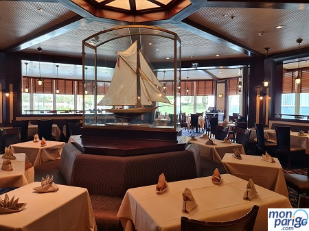 Mesas con servilletas y una gran maqueta de un velero en el comedor del restaurante Yacht club del hotel Newport Bay Club de Disneyland Paris